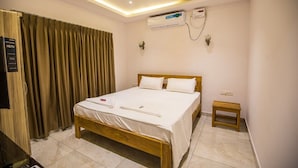 A hotel room with a wooden bed, white bedding, a small wooden stool, an air conditioning unit, and a ceiling light. - Forest View farmhouse stay (Kosiyakutoli)