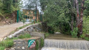 A small waterfall in a natural setting with a green gate and a sign in the foreground. - Forest View farmhouse stay (Kosiyakutoli)