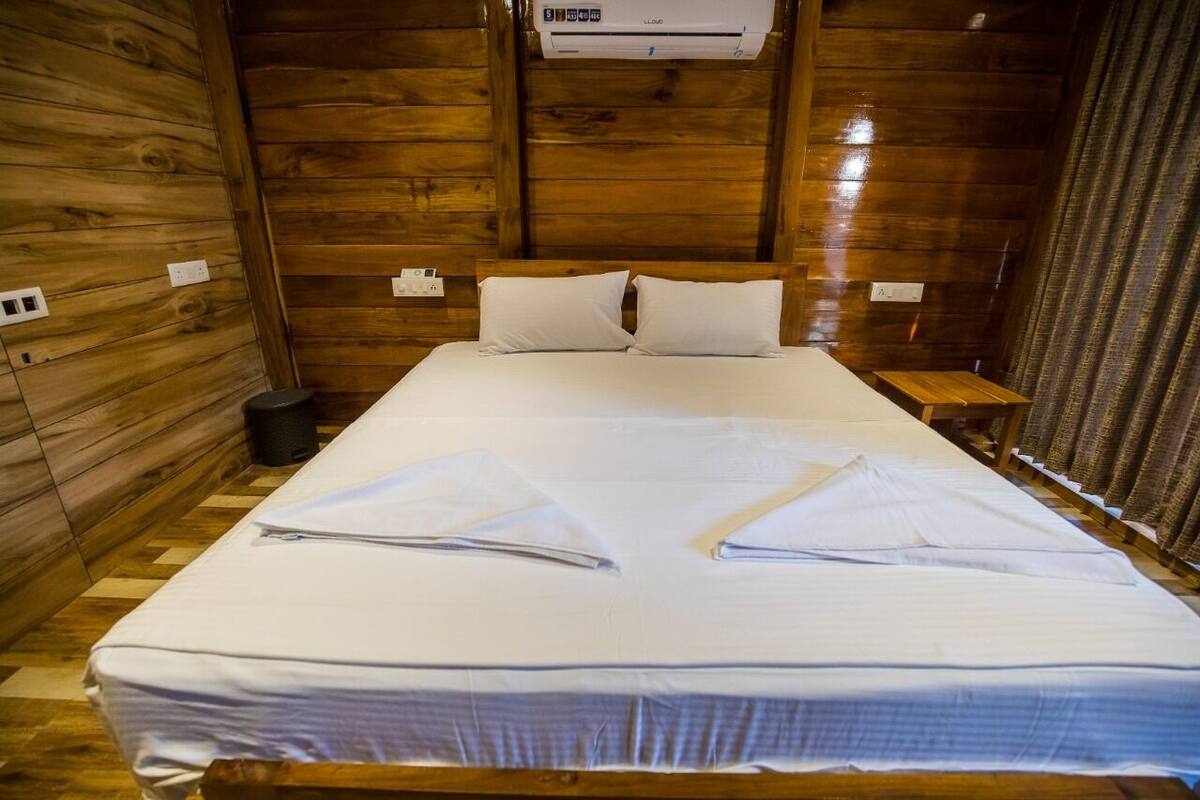 A wooden cabin room with a bed, a small bedside table, and an air conditioning unit.