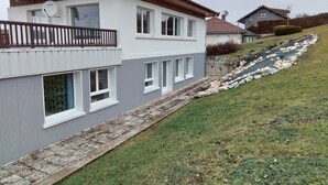 A modern two-story house with a grey facade, white windows, and a balcony. - Apartment 3 (Longchaumois)
