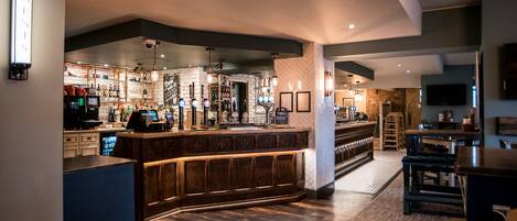 Zona moderna de bar con mostrador de madera, múltiples grifos de cerveza y un área de estar con taburetes de bar.