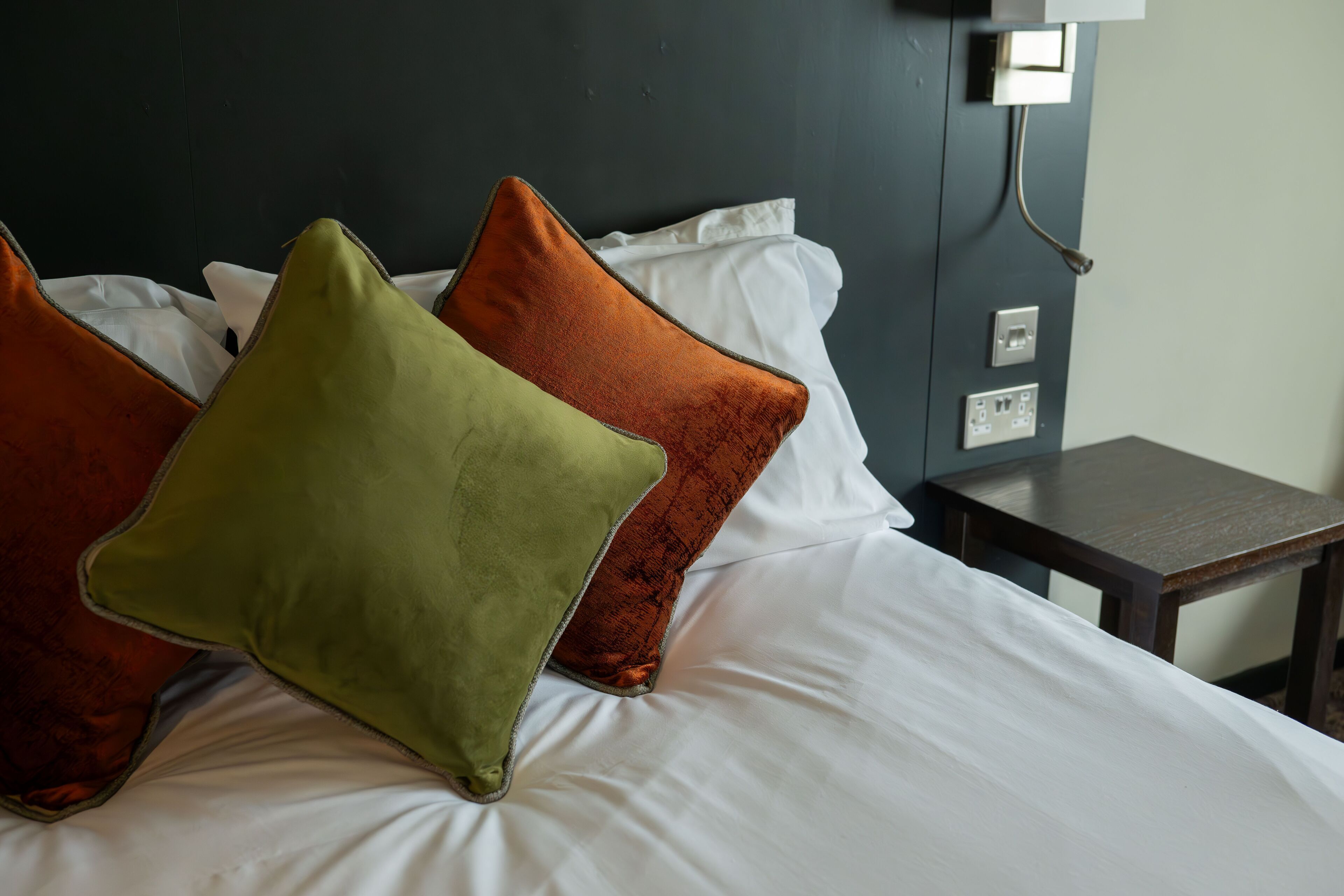 Una cama con sábanas blancas y varias almohadas de diferentes colores.