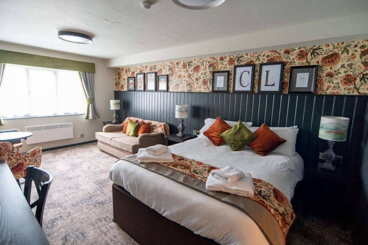 A hotel room with a large bed, two armchairs, a dining table, and a window with curtains.