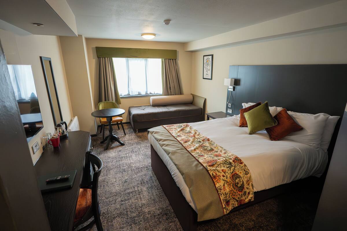 A hotel room with a bed, a desk, a chair, a sofa, and a window with curtains.