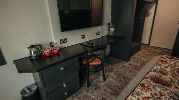 Une chambre d’hôtel de taille modeste, dotée d’un bureau en bois foncé, d’une seule chaise, d’un grand miroir, d’une télévision et d’une couvre-lit à motifs.