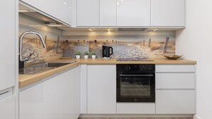 Una cocina moderna con armarios blancos, encimera de madera, lavavajillas integrado y salpicadero decorado con motivos playeros.