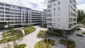 Un edificio moderno de varios pisos con una fachada curva, rodeado de zonas ajardinadas con árboles y senderos.