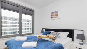 Un dormitorio moderno con una cama grande, una mesita de noche con lámpara y una ventana con persianas.