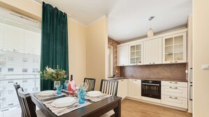 A dining area with a table set for four, a kitchen with white cabinets, and a window with blinds. - Spacious Apartment | Balcony, Parking, Workspace (Wroclaw)