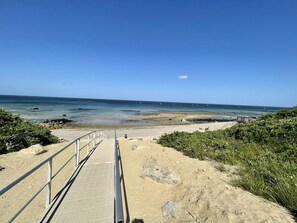 A beach with a wooden walkway leading to the shore, surrounded by greenery.