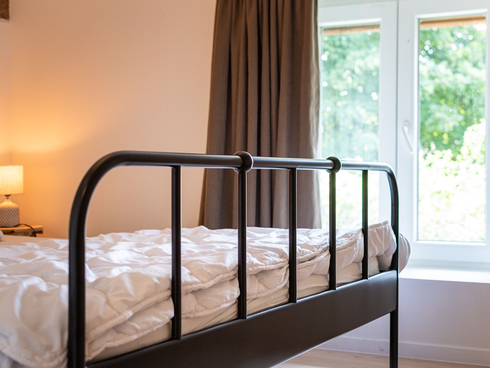 A bed with a metal frame and white bedding in a room with a window and curtains.