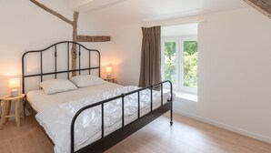 Une chambre à coucher avec un lit, des lampes de chevet, une fenêtre avec des rideaux et des poutres apparentes.