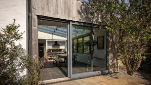 A modern house with a glass door leading to a patio area with a table and chairs.