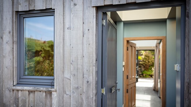 A wooden door with a window, a hallway with wooden doors, and a view of greenery outside.