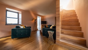 A spacious living room with two dark sofas, a round glass table, and a wooden staircase.