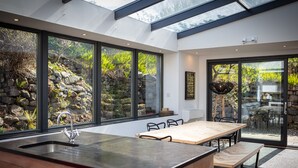 A modern kitchen with a large island, built-in appliances, and large windows offering views of a garden and outdoor seating area.