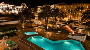 Nachtsicht eines Hotels mit zwei Schwimmbecken, Liegestühlen und Palmen.