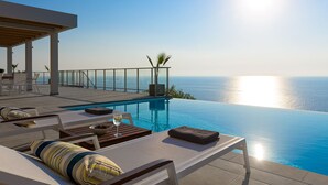 Une piscine à débordement offrant une vue imprenable sur l’océan, des chaises longues et un espace salon abrité.