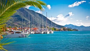 Un port de plaisance avec des bateaux amarrés, un paysage montagneux en arrière-plan et un ciel bleu dégagé.