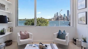 Ein modernes Wohnzimmer mit zwei weißen Sofas, einem Couchtisch und einem großen Fenster mit Blick auf die Stadtlinie.