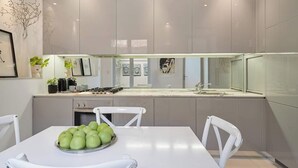 Eine moderne Küche mit grauen Schränken, einem weißen Esstisch mit Stühlen und einer Obstschale.
