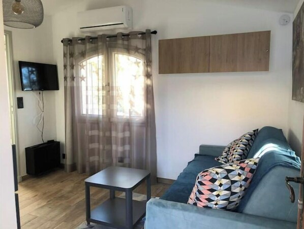 A living room with a sofa, a small table, a TV, and a window with curtains.