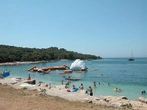 A beach with people swimming and sunbathing, boats, and a sailboat in the distance. - Mobile home with air conditioning and terrace (Pula)