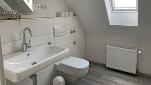 Une salle de bain moderne avec un lavabo, des toilettes et un radiateur, le tout de couleur blanche.
