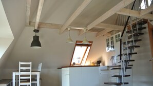 Une cuisine avec un îlot central blanc, des poutres en bois et un escalier en colimaçon.