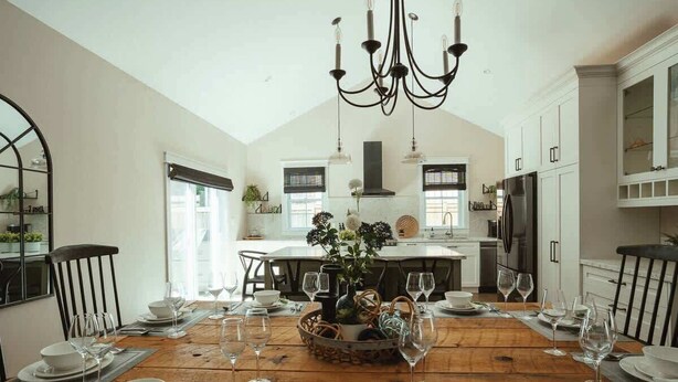 A dining area with a wooden table set for a meal, a chandelier, and white cabinetry. - Beach House 5 Star Gem +Muskoka room + Yoga Studio (Innisfil)