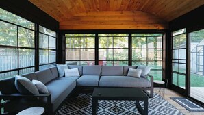 A modern living room with a sectional sofa, a coffee table, and large windows offering a view of the backyard. - Beach House 5 Star Gem +Muskoka room + Yoga Studio (Innisfil)
