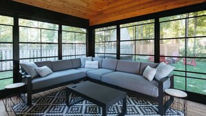 A covered outdoor seating area with a sectional sofa and a coffee table, large windows, and a patterned rug. - Beach House 5 Star Gem +Muskoka room + Yoga Studio (Innisfil)
