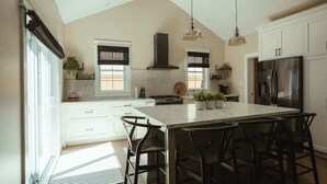 A modern kitchen with a large island, white cabinetry, and pendant lighting. - Beach House 5 Star Gem +Muskoka room + Yoga Studio (Innisfil)