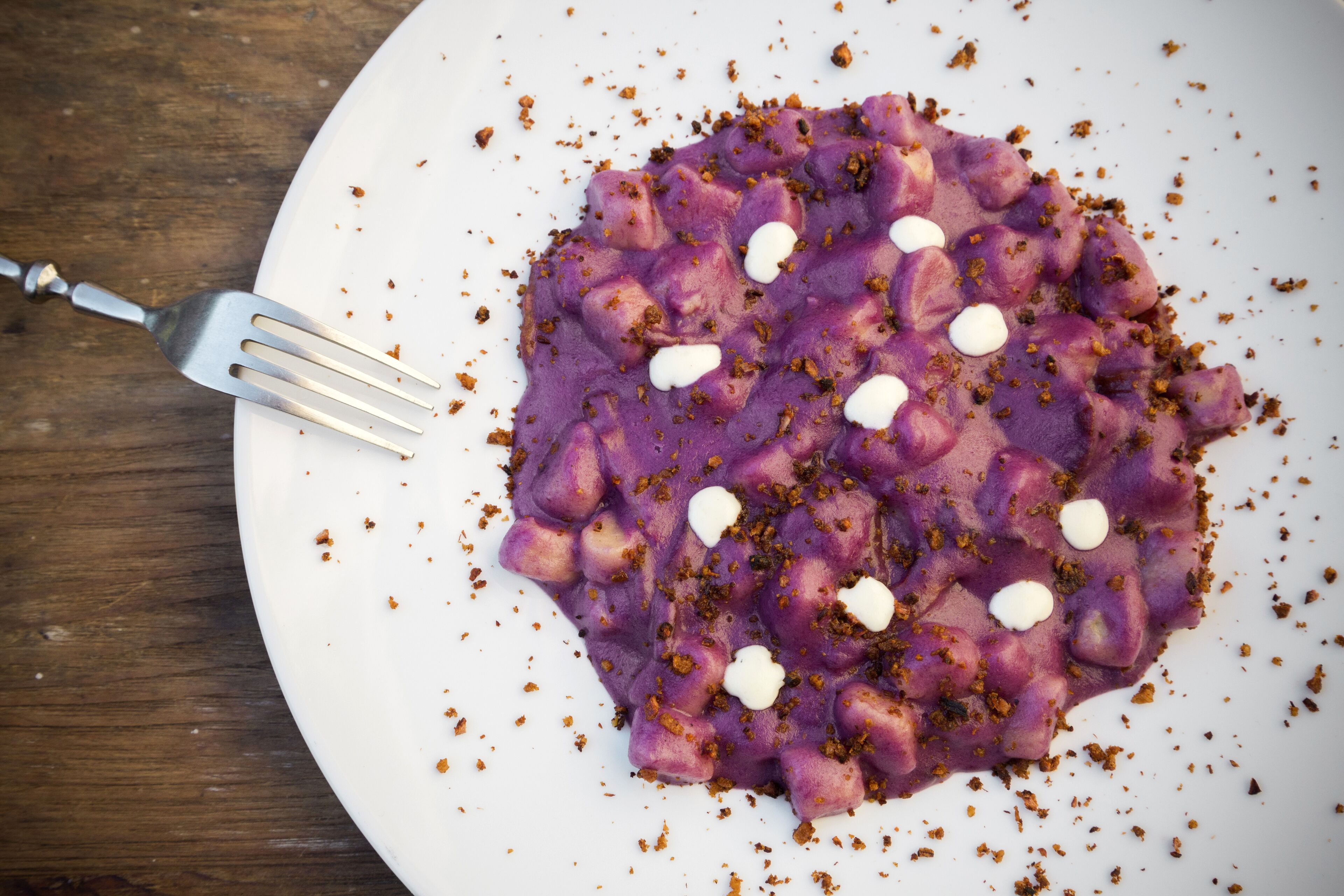 A plate of purple food with white dollops and crumbs on a white plate.