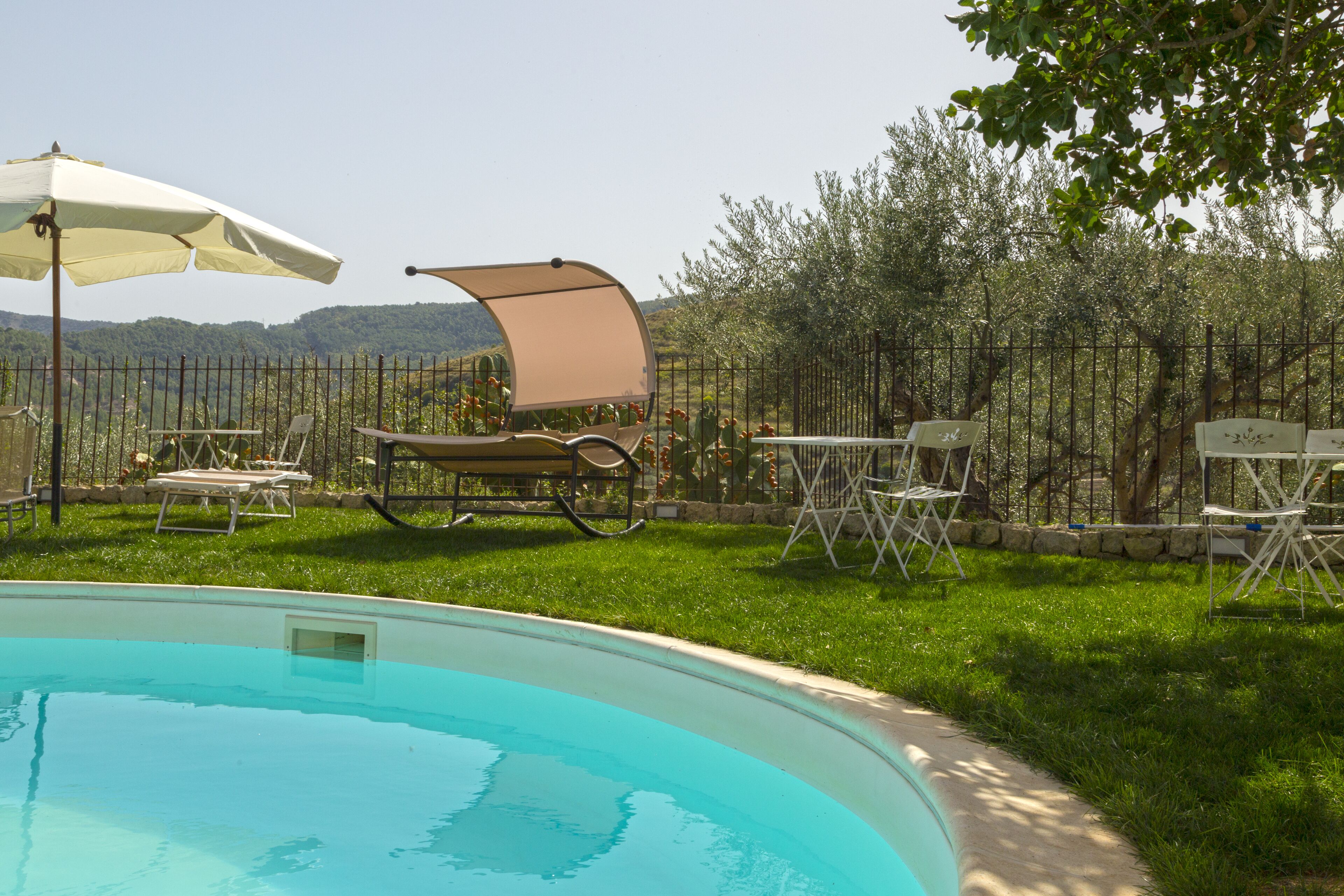 A swimming pool with a grassy area, lounge chairs, and a table with a canopy.