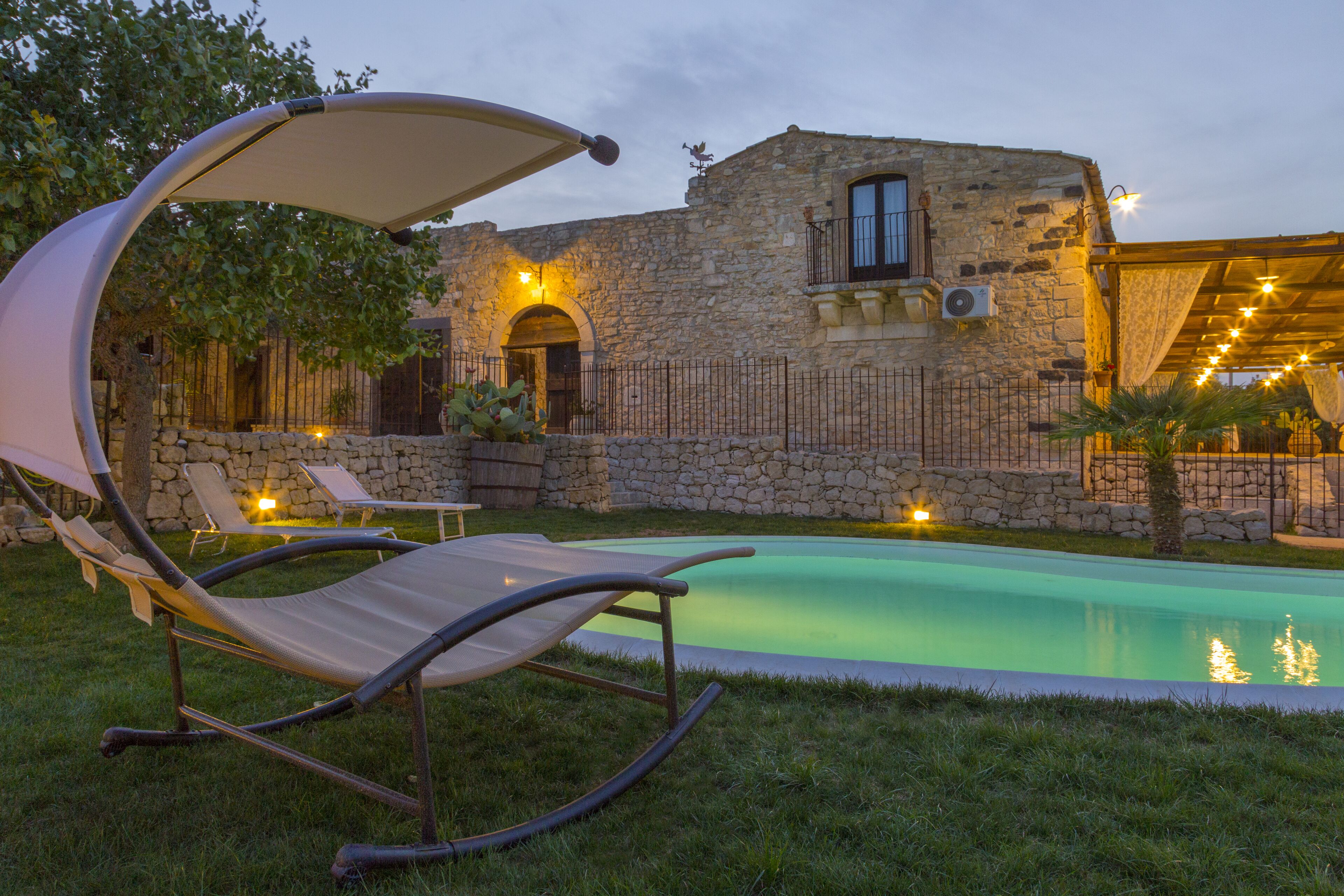 Ein Gebäude aus Stein mit Pool, einer Hängemattenliege und einer Pergola mit Beleuchtung.