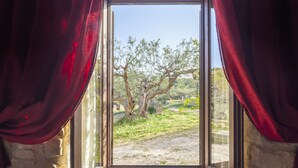 An open window with red curtains, revealing a view of a tree and a stone wall. - Masseria Fortificata Lo Zafferaneto  (Buccheri)