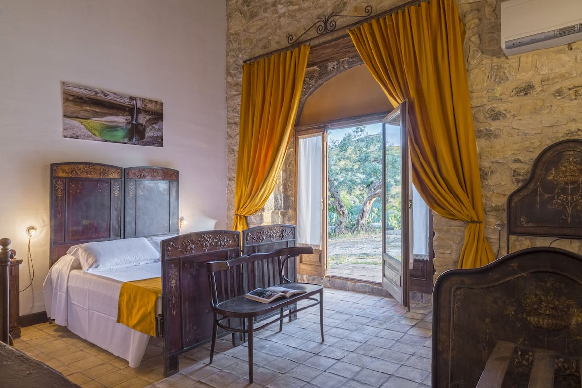A bedroom with a bed, a bedside table, a chair, and a window with curtains.