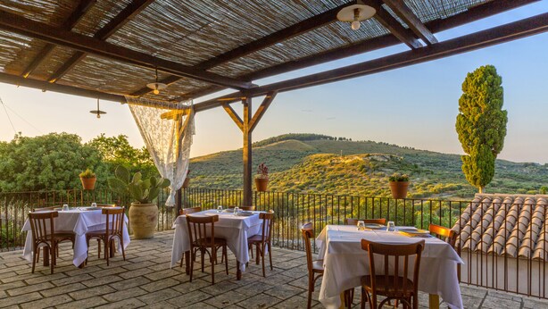An outdoor patio with tables and chairs, a pergola, and a view of hills. - Masseria Fortificata Lo Zafferaneto  (Buccheri)