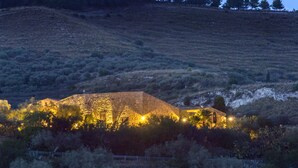 A stone building with a sloped roof, surrounded by dense shrubbery and trees, under a twilight sky. - Masseria Fortificata Lo Zafferaneto  (Buccheri)