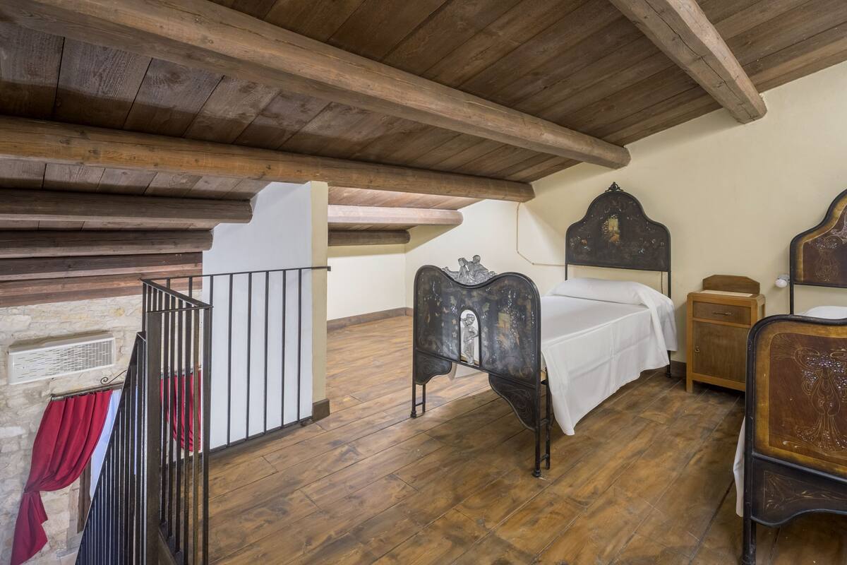 A bedroom with a wooden ceiling, a bed with a headboard, a nightstand, and a wooden floor.