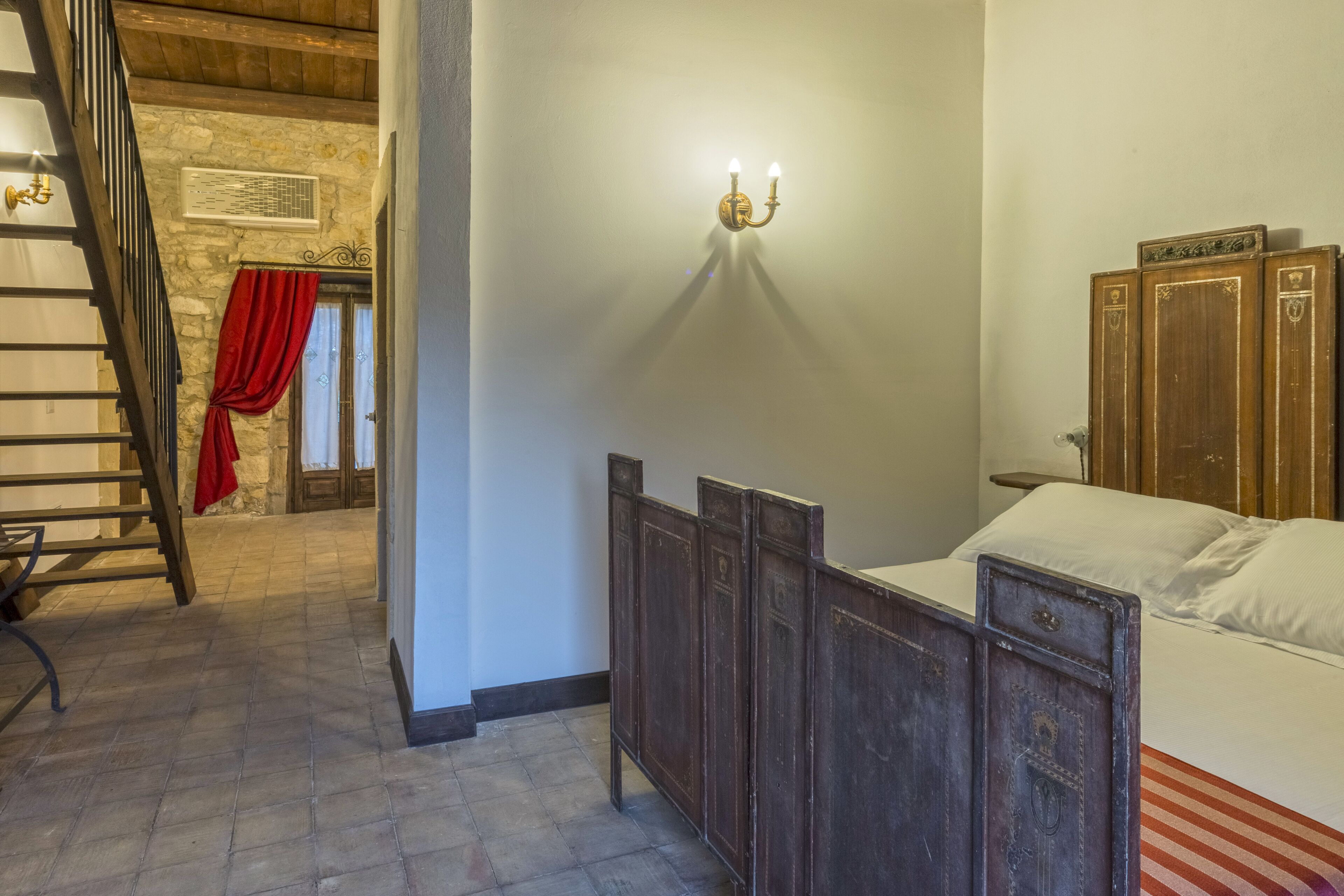 Ein Schlafzimmer mit einem hölzernen Bett, einem Nachttisch, einer Wandleuchte und einer Treppe, die zu einem anderen Raum führt.