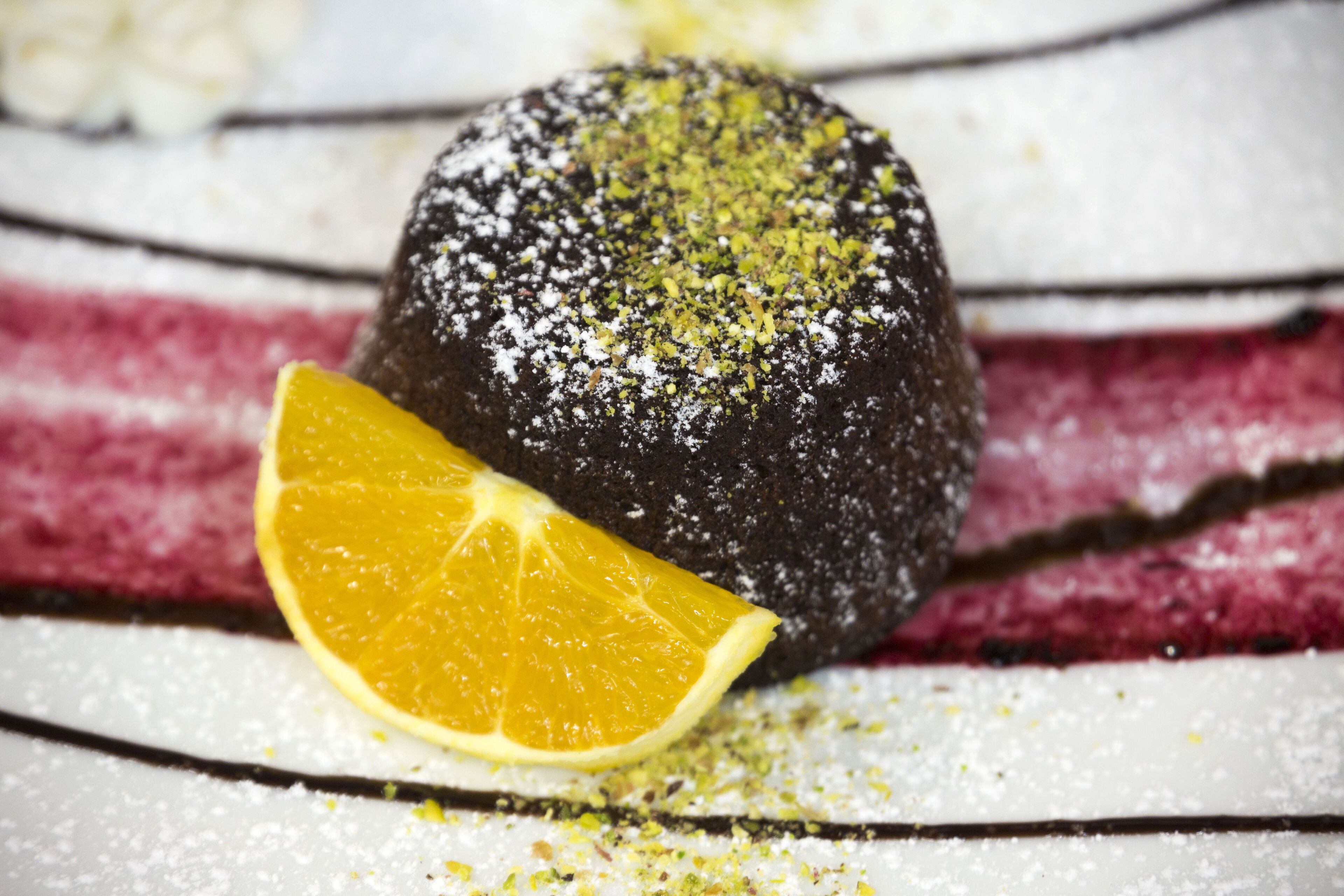 A dessert with a slice of orange on top, dusted with powdered sugar and green garnish, on a striped surface.
