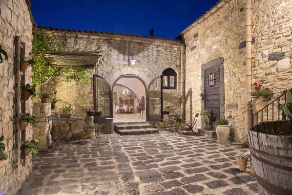 A stone courtyard with a wooden bench, potted plants, and a view into a building with a wooden door. - Masseria Fortificata Lo Zafferaneto (Buccheri)