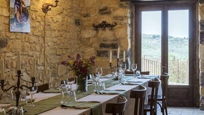 A dining area with a stone wall, a table set for six with candles, and a view of the countryside through a large window. - Masseria Fortificata Lo Zafferaneto  (Buccheri)