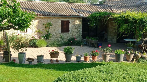 A stone building with a tiled roof, surrounded by potted plants and a grassy area.