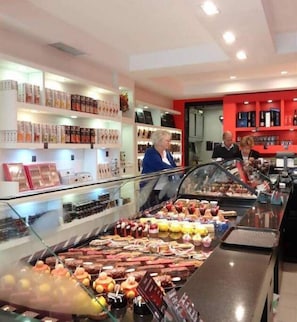 Vitrine de padaria com diversos produtos de panificação e uma pessoa ao fundo.