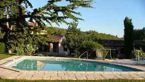 A rectangular swimming pool with a tiled deck, surrounded by a well-maintained lawn and trees.