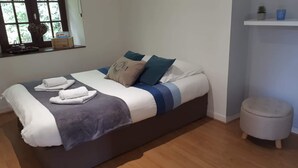 A modern bedroom with a large bed, a bedside table, a small stool, and a window with a view of greenery.