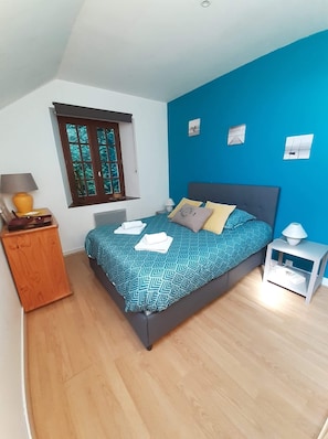 Une chambre à coucher avec un lit, une table de chevet, une armoire en bois, une fenêtre et un mur bleu.